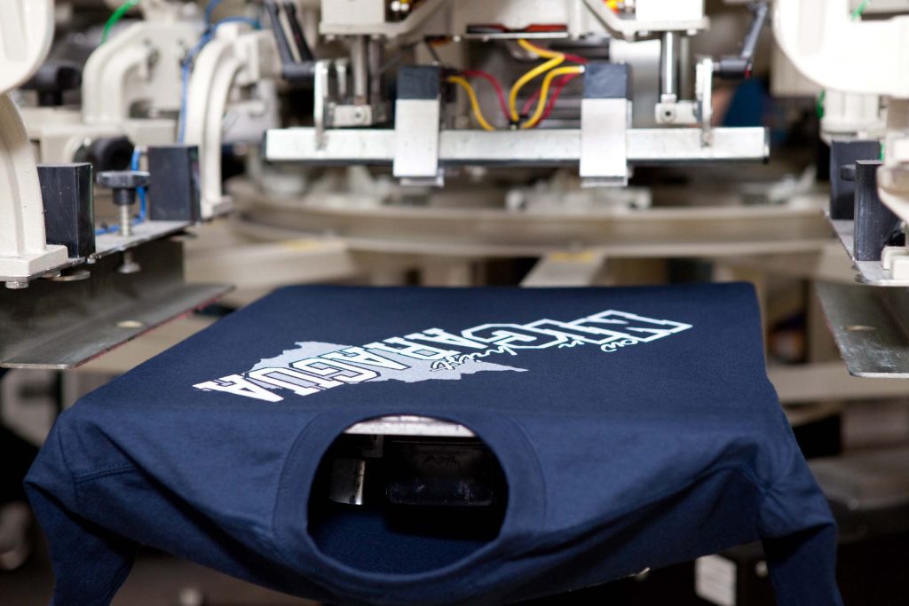 A t-shirt being printed with a white design on a blue fabric.