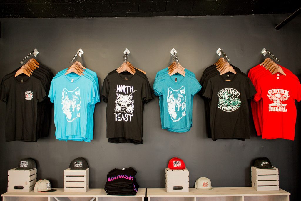 Four graphic t-shirts hanging on a wall with various designs and text.